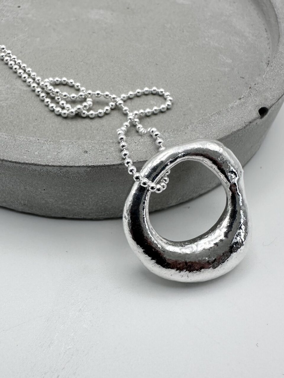 Handcrafter molten silver organc pendant necklace on a silver ball chain, textured and hallmarked artisan jewellery.