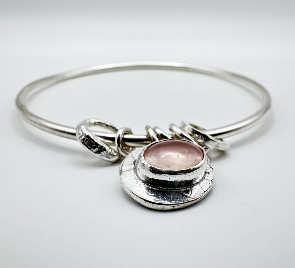 Handmade sterling silver bangle with rose quartz charm on wrist – artisan jewellery by Bohdee.”